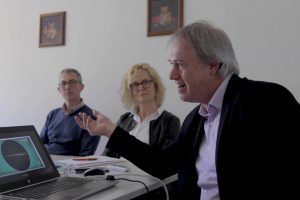 Docente che tiene un corso di lingua in presenza con partecipanti adulti in aula, davanti a un laptop con una presentazione