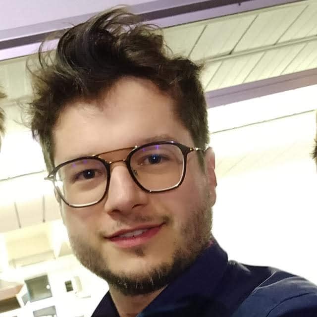 Ritratto di un giovane con occhiali in un ambiente interno.