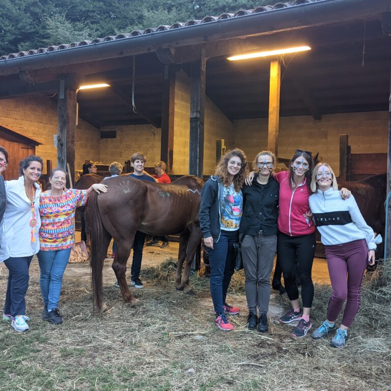 Gruppo di donne sorridenti in un maneggio con cavalli.