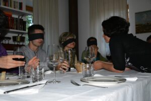 Partecipanti a un corso di lingua seduti a un tavolo con bende sugli occhi.